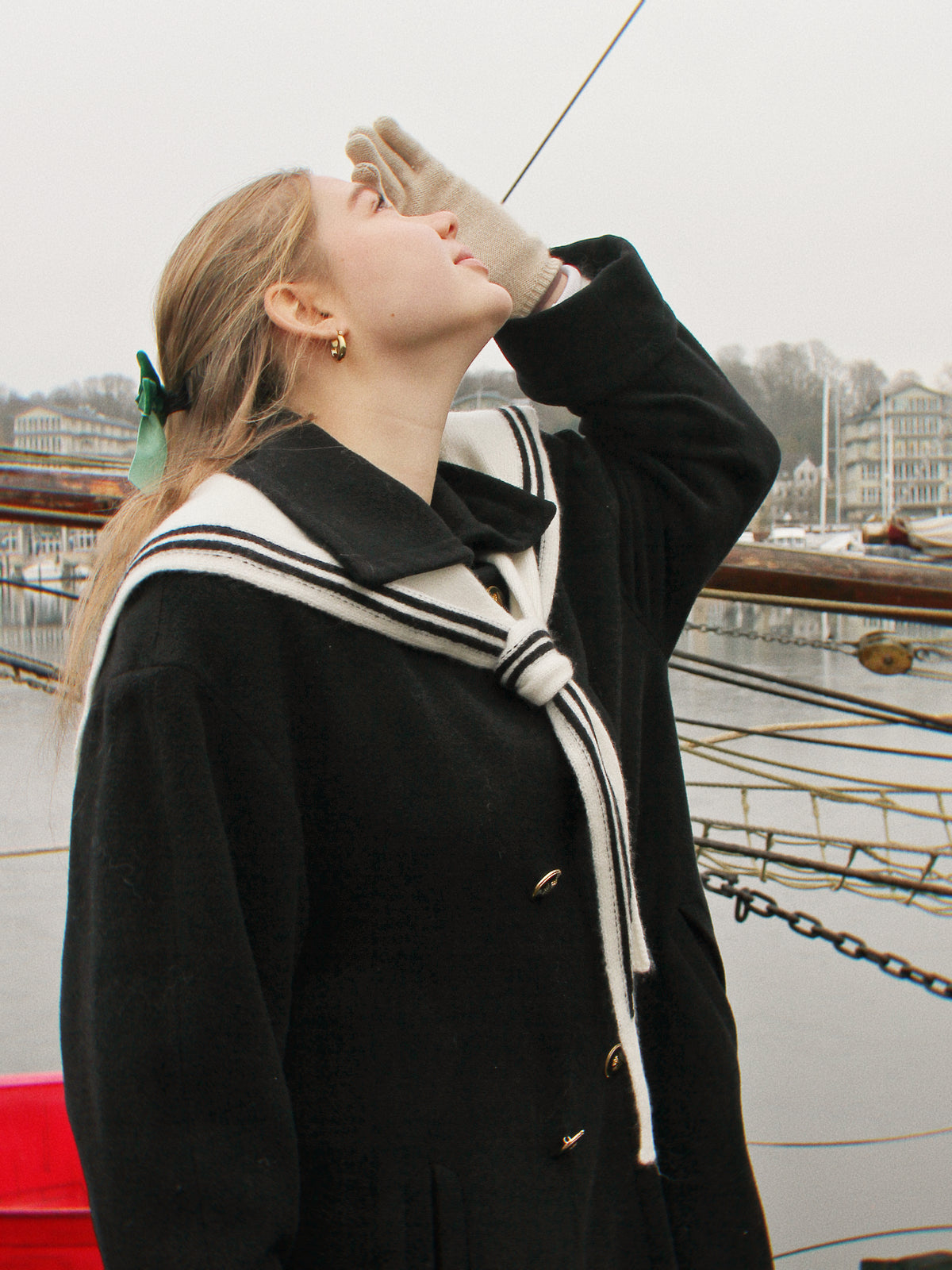 Aglaea Studio Nautischer Schal aus Merinowolle mit Streifen Model blickt in die Ferne an einem klassischen Segelschiff